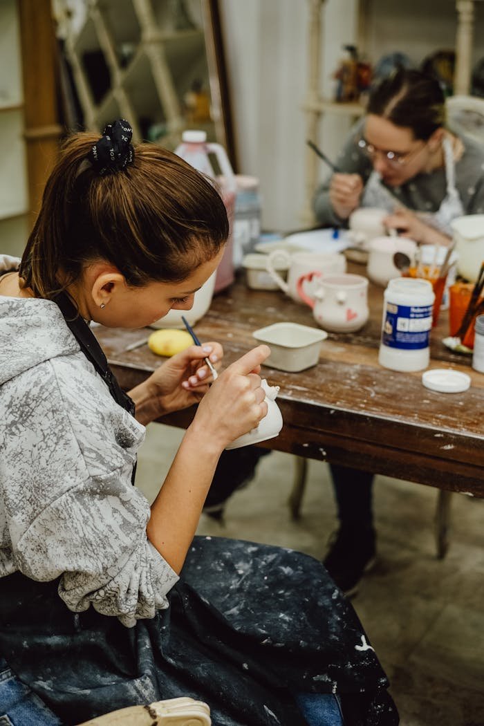 Two women painting ceramics in a creative pottery workshop setting.