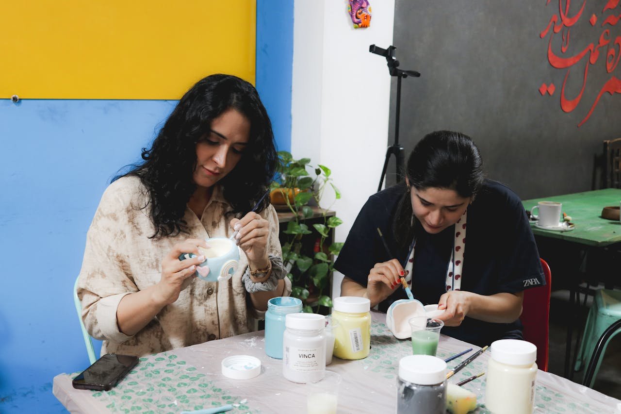 Two women engaged in painting ceramics at a creative workshop indoors.
